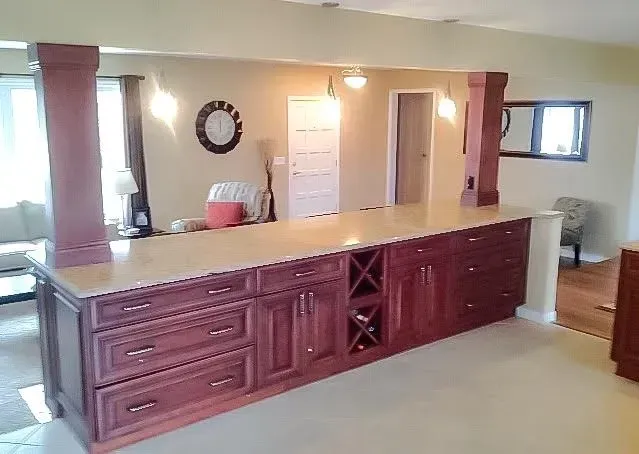 A long, dark-stained wood kitchen island with a light countertop, flanked by two matching pillars in an open living space.