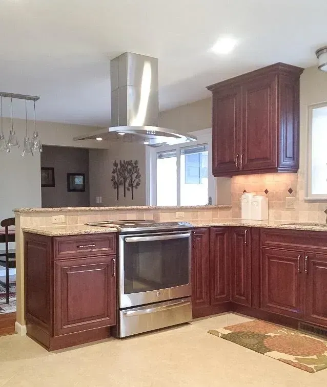 A kitchen with dark wood cabinets, stainless steel appliances, a range hood, and light granite countertops.