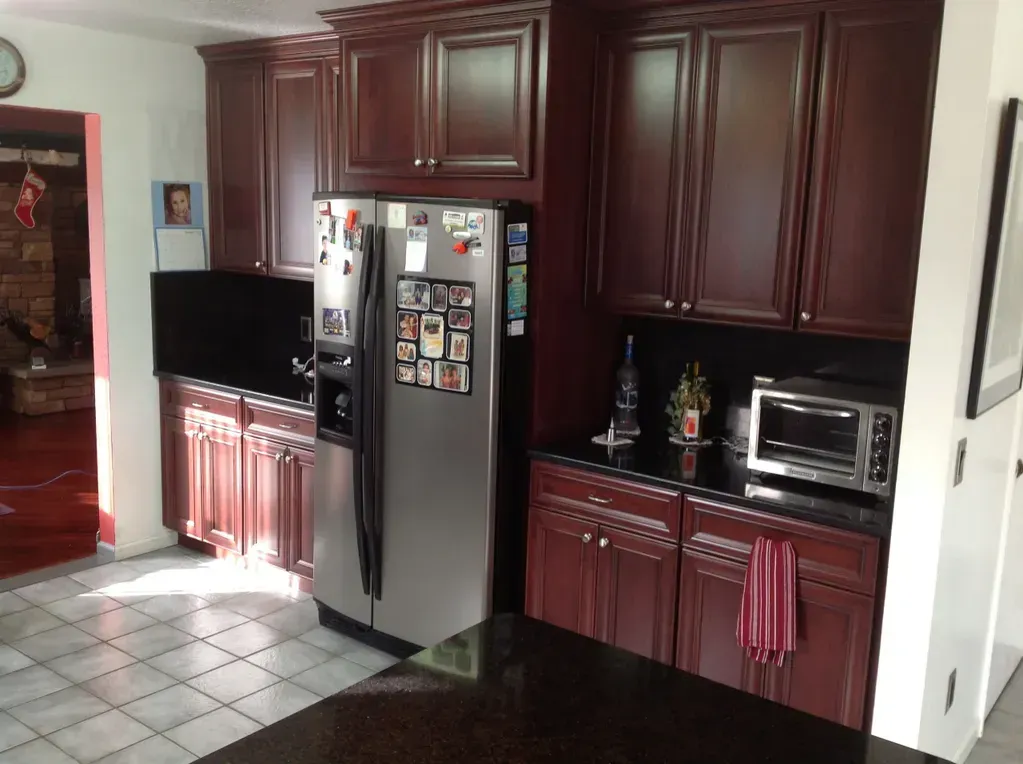 A kitchen with cherry wood cabinets, black countertops, stainless steel appliances, and a tiled floor.