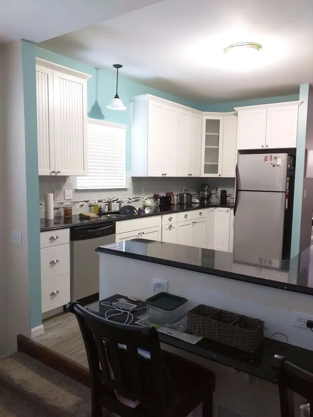 A kitchen with white cabinets, light blue walls, a dark countertop, stainless steel refrigerator, and breakfast bar.