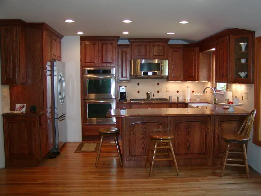A spacious, wood-cabinet kitchen with stainless steel appliances, a center island with three stools, and hardwood floors.