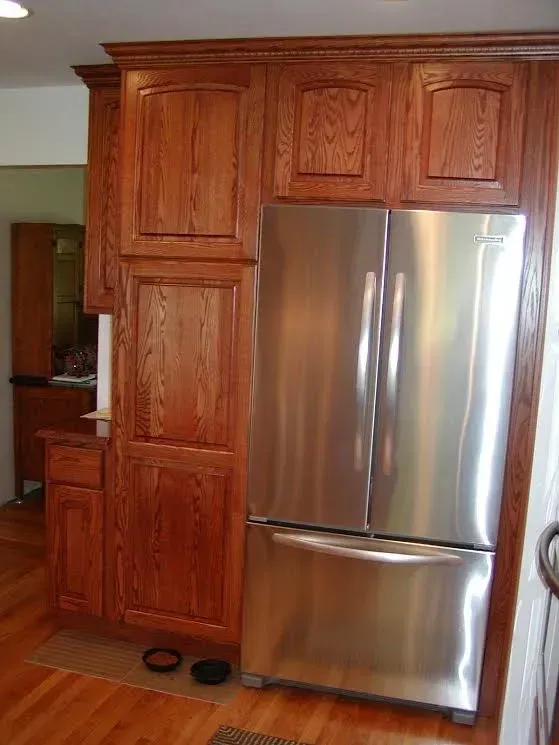 A stainless steel French-door refrigerator built into custom wooden cabinetry in a kitchen with wood flooring.