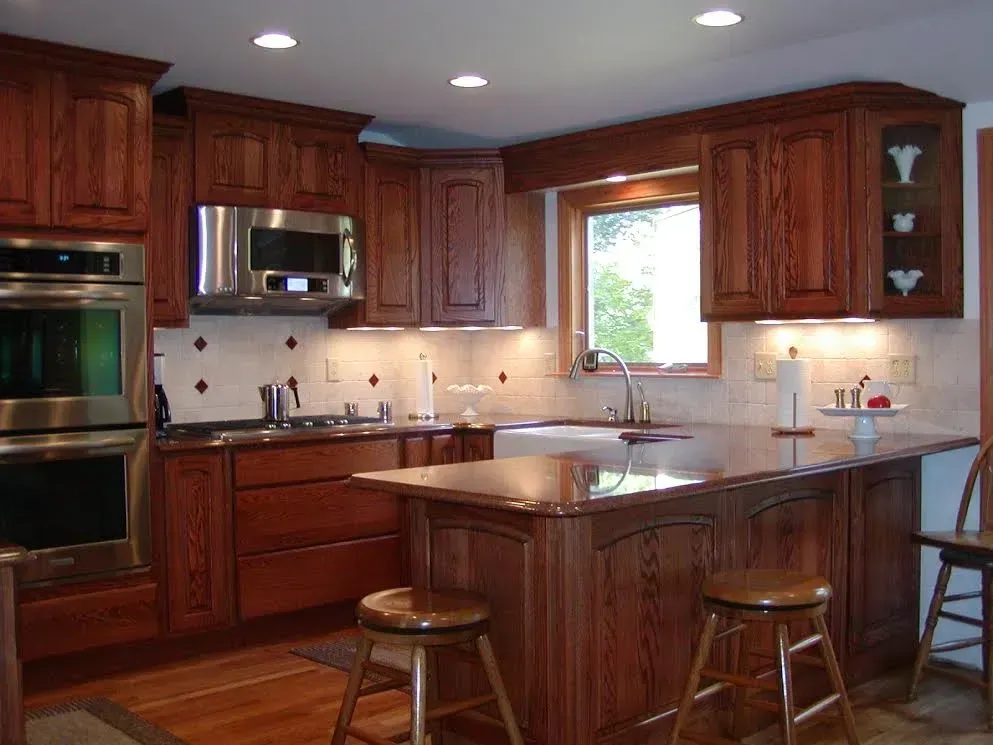 A traditional kitchen with stained wood cabinets, granite countertops, stainless steel appliances, and two wooden stools.
