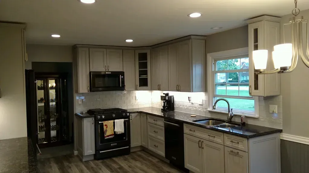 A kitchen featuring light-gray cabinets, dark countertops, black appliances, recessed lighting, and a window over the sink.