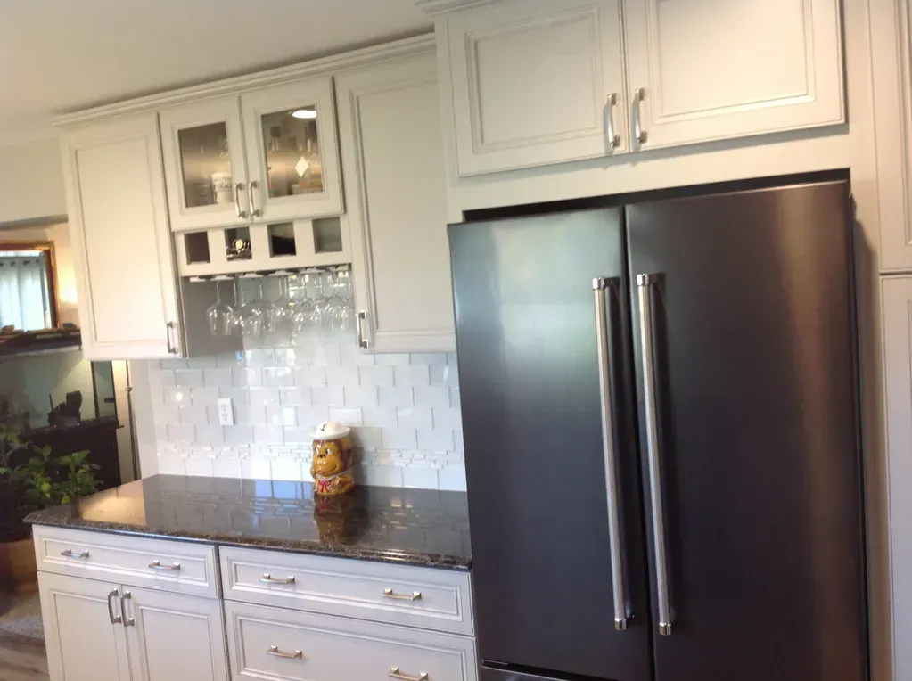 A modern kitchen featuring white cabinets, a dark granite countertop, a glass-front wine rack, and a dark stainless fridge.