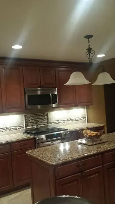 A kitchen with dark wood cabinets, granite countertops, a stainless steel microwave and oven, and pendant lights.