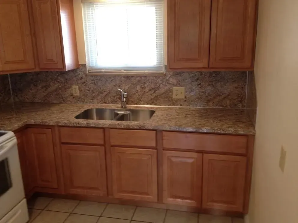 Kitchen counter with medium-brown wood cabinets, granite countertops, a stainless steel sink, and a window.