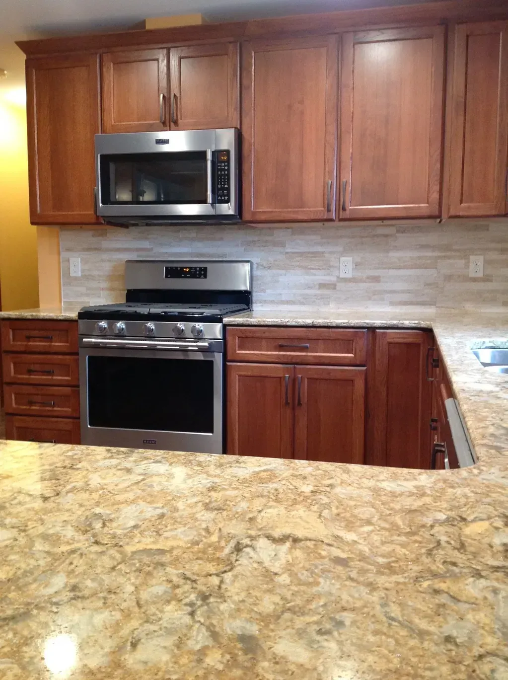 A modern kitchen featuring wooden cabinets, a stainless steel oven and microwave, and a textured, stone-look countertop.