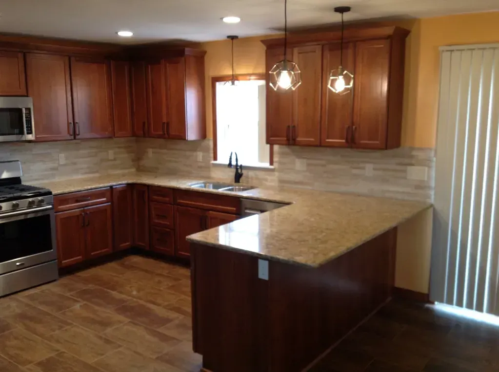 A modern kitchen with cherry wood cabinets, granite countertops, stainless steel appliances, and tile backsplash.