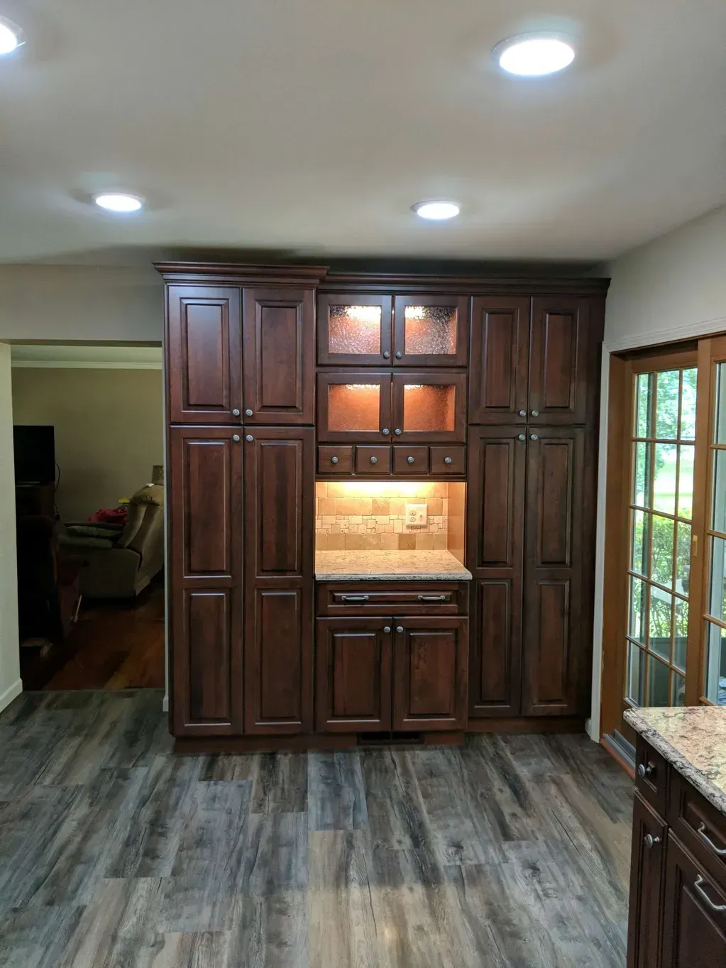 A large, dark wood cabinetry unit with glass-front display shelves and a stone countertop, set in a kitchen.