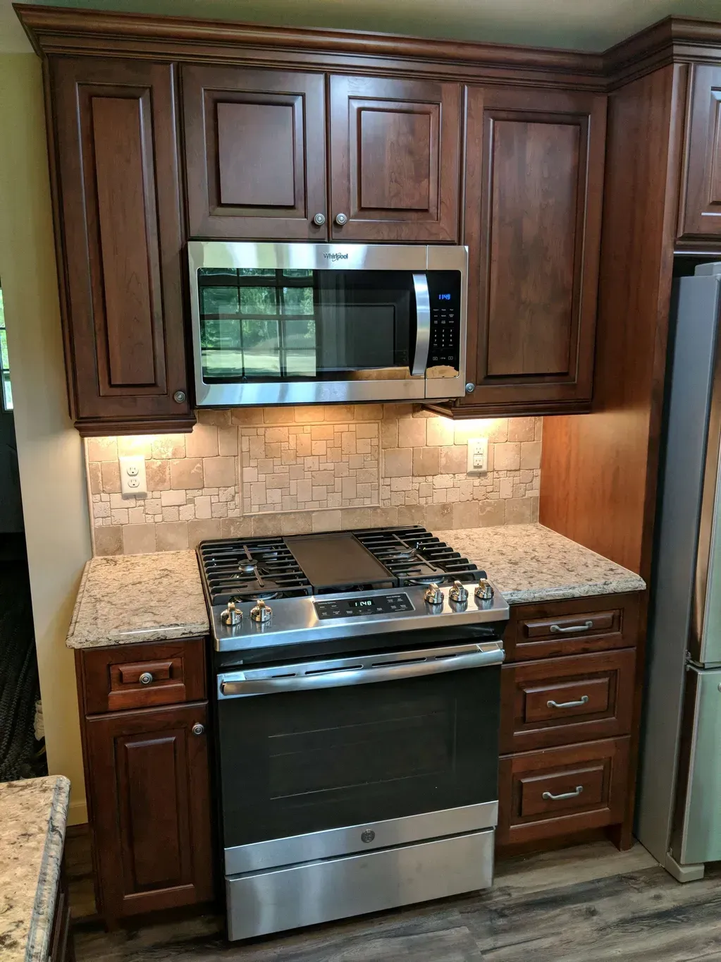 Kitchen area featuring dark wood cabinets, a stainless steel stove and microwave, and a textured stone tile backsplash.