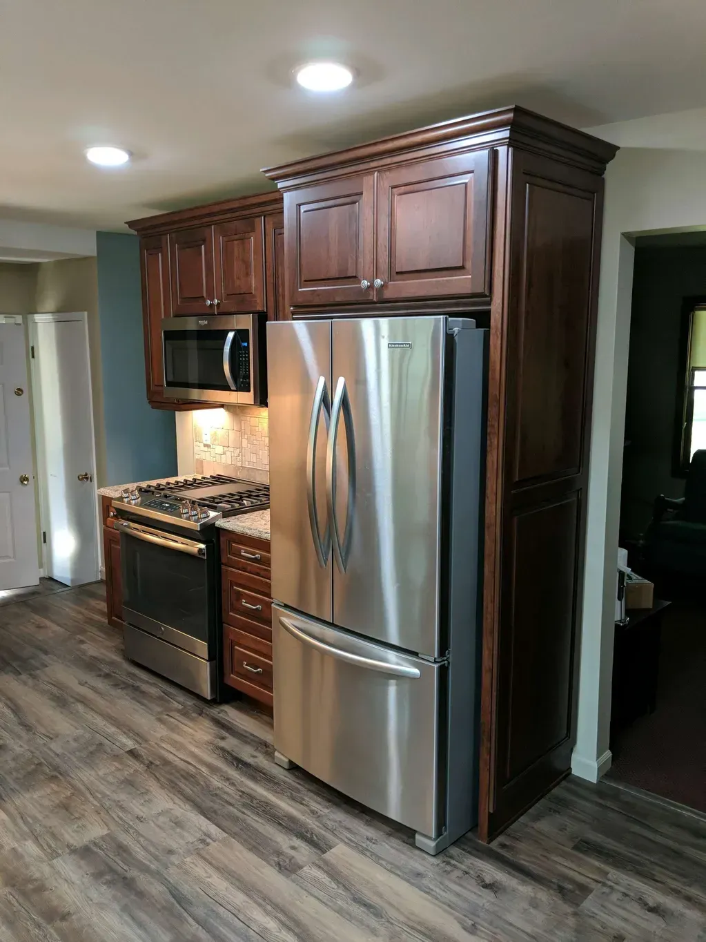 Modern kitchen with stainless steel appliances, dark wood cabinets, and light wood-look flooring.