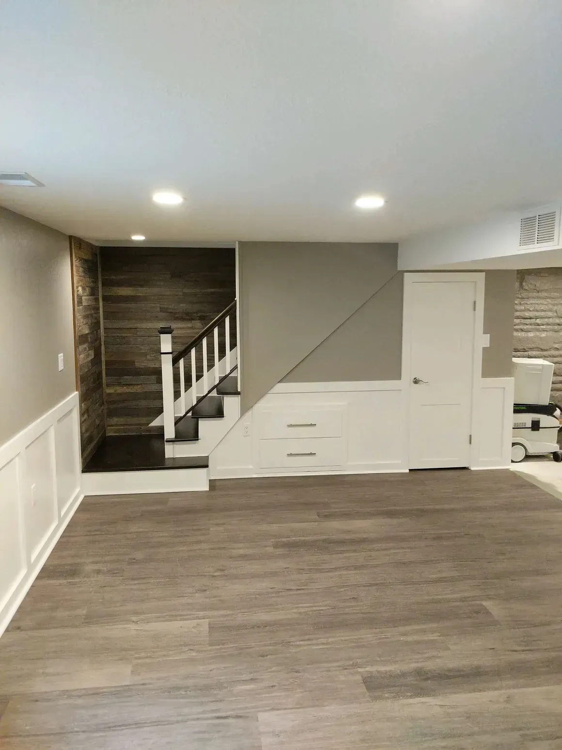 A renovated basement room featuring a staircase with wood-paneled walls, built-in storage under the stairs, and wood floors.