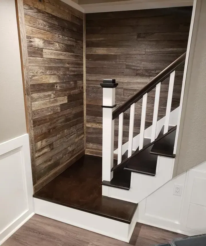 A staircase with dark wood treads and a white railing, set against a corner wall featuring rustic, weathered wood planks.