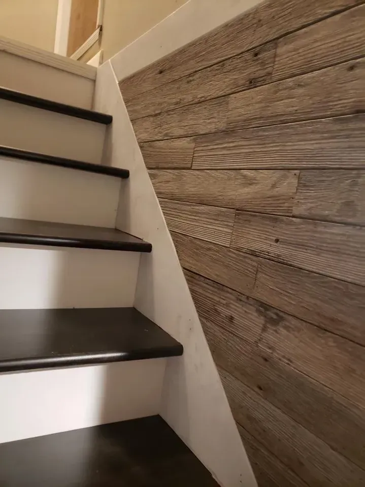 A staircase featuring dark wood treads, white risers, and a diagonal accent wall paneled in rustic, weathered wood planks.