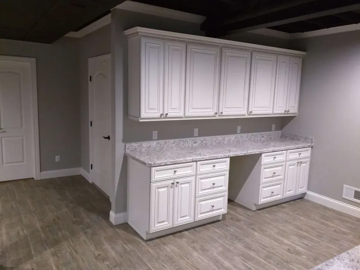 White kitchen cabinets with granite countertops and light wood-look flooring in a room with gray walls.