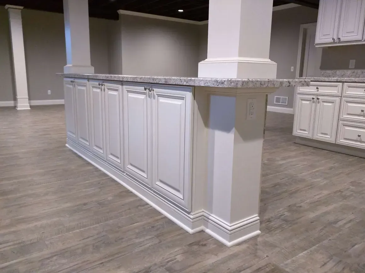 A kitchen island with white cabinets and a granite countertop, situated on light-toned wood-look flooring.