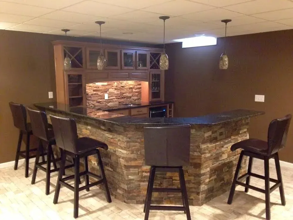 A home basement bar with a stone facade, dark wood cabinets, four leather stools, and pendant lighting.
