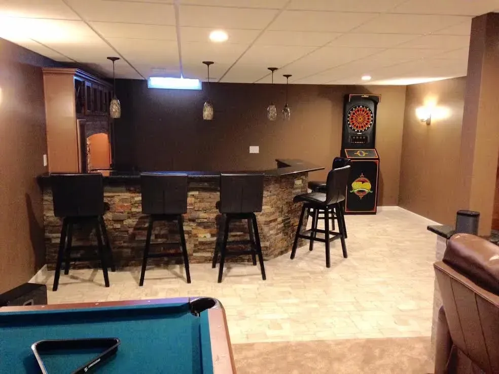 A basement bar with stone siding, four stools, three pendant lights, a dartboard, and a partial view of a pool table.