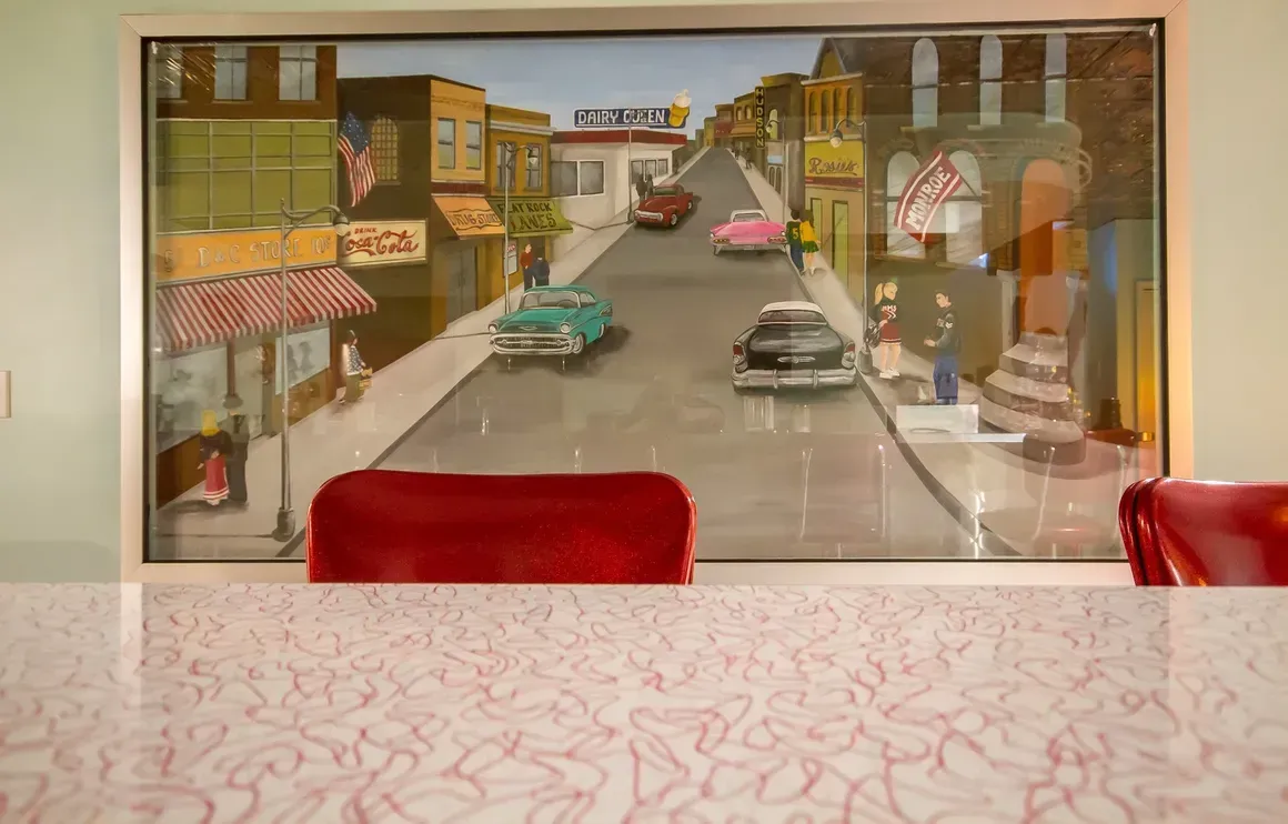 A retro-style countertop with a patterned top sits below a framed painting of a street scene featuring vintage cars.