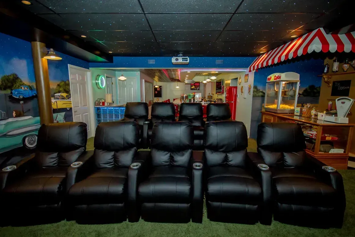 A home theater room with two rows of black leather reclining chairs, a popcorn machine, and a starry night ceiling mural.