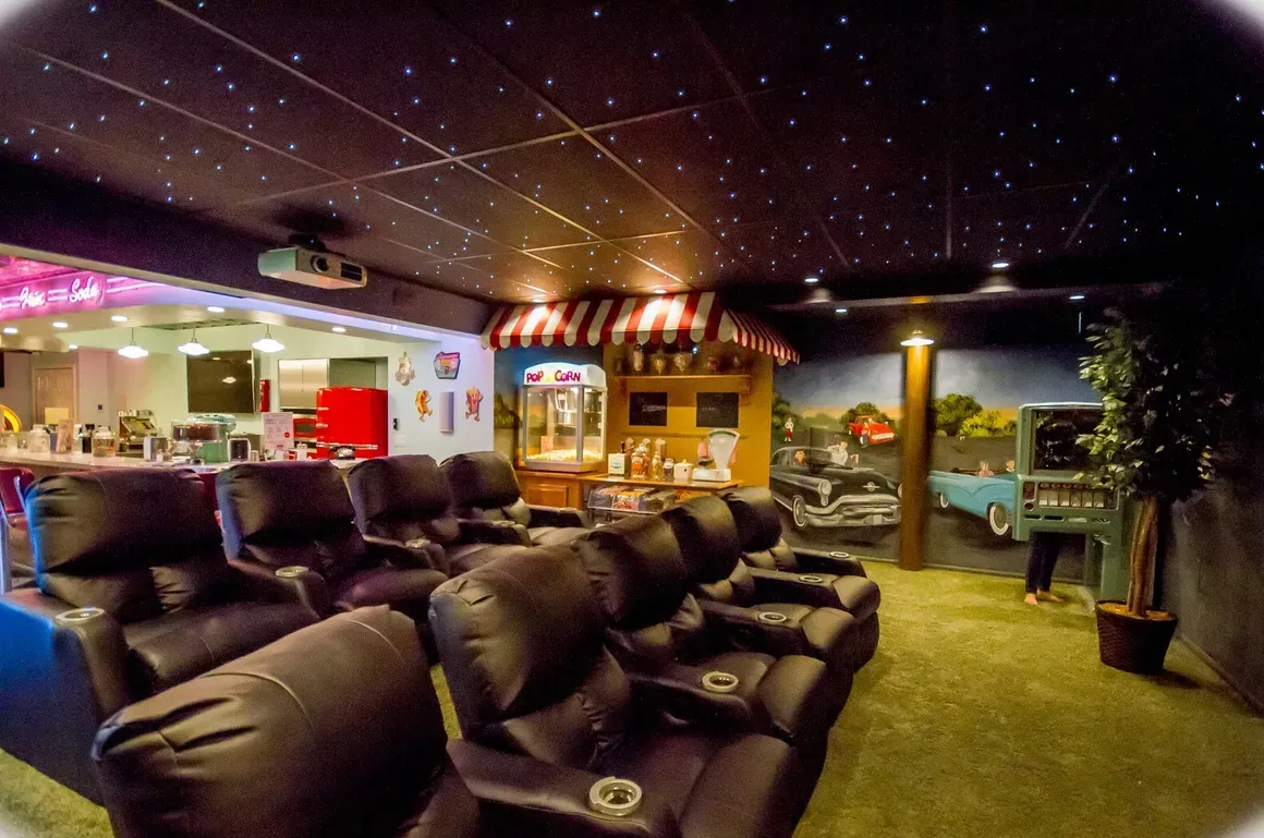 A home theater room with rows of black leather recliners, a starlit ceiling, a popcorn machine, and mural-covered walls.