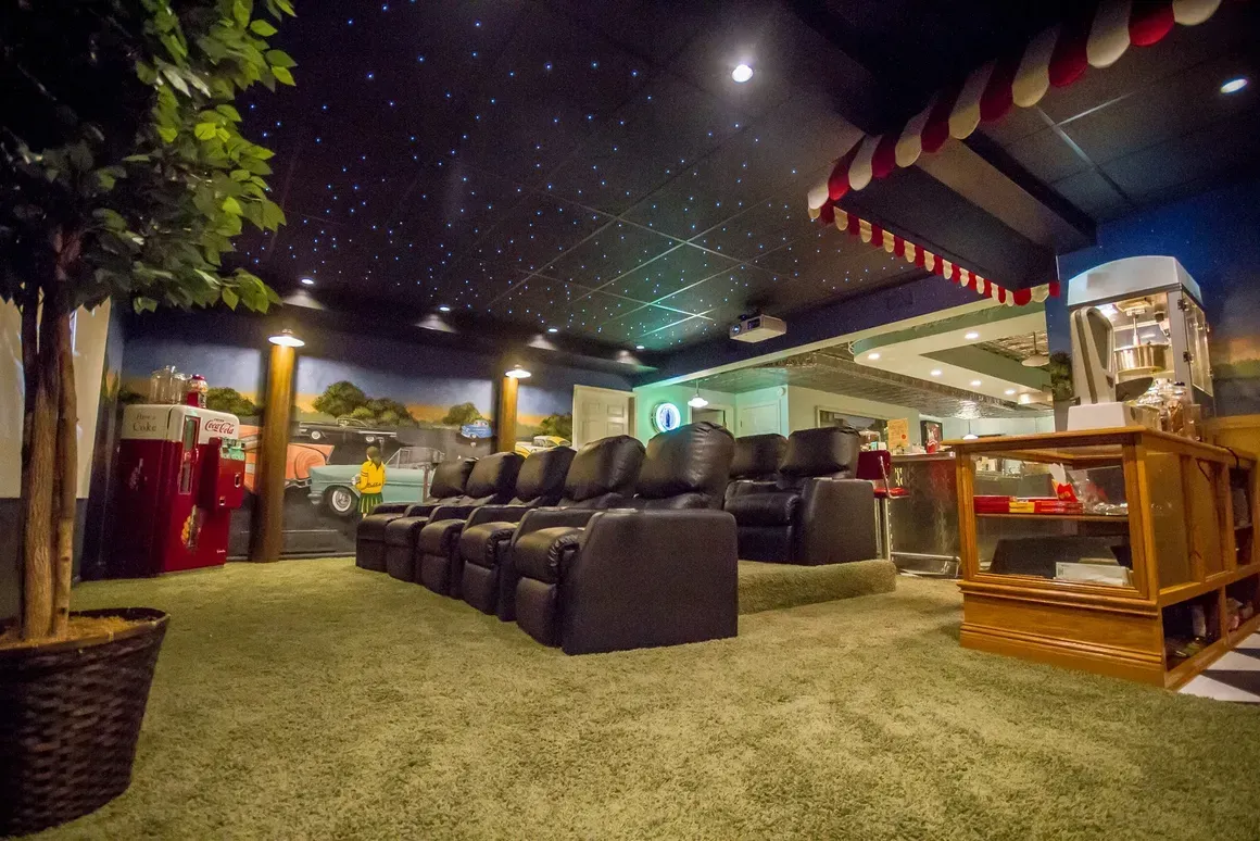 A themed home theater with rows of black reclining chairs, a starry night ceiling, artificial grass, and a snack stand.
