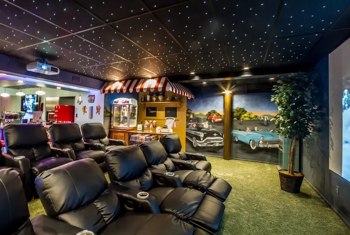 A home theater with rows of black leather recliners, a starry night ceiling, and a vintage-themed wall mural.