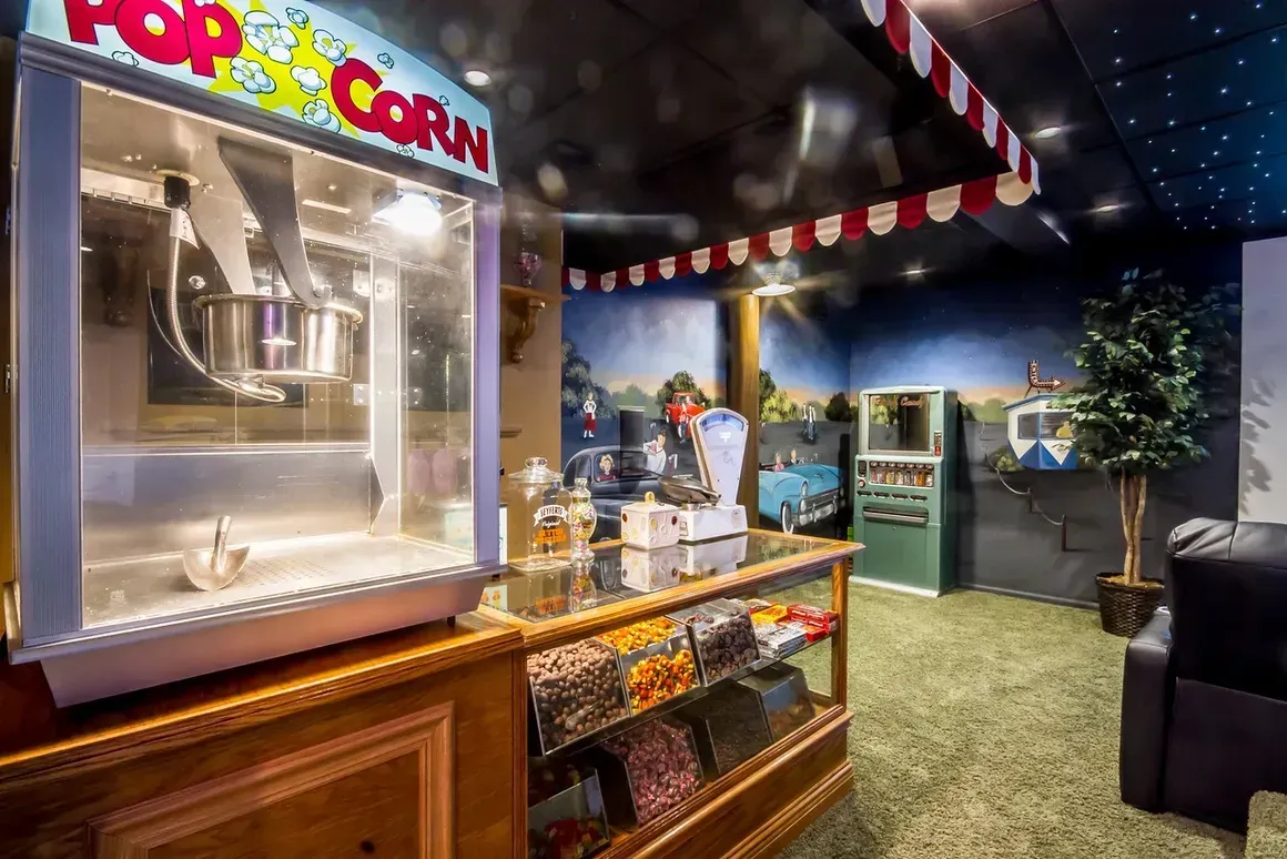 A home theater snack bar with a popcorn machine, a glass candy case, retro decor, and a movie-themed mural.