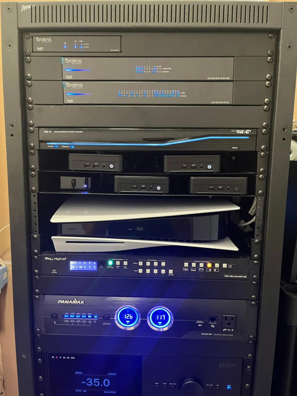 Rack of audio/AV equipment with glowing blue indicators and stacked components in a cabinet