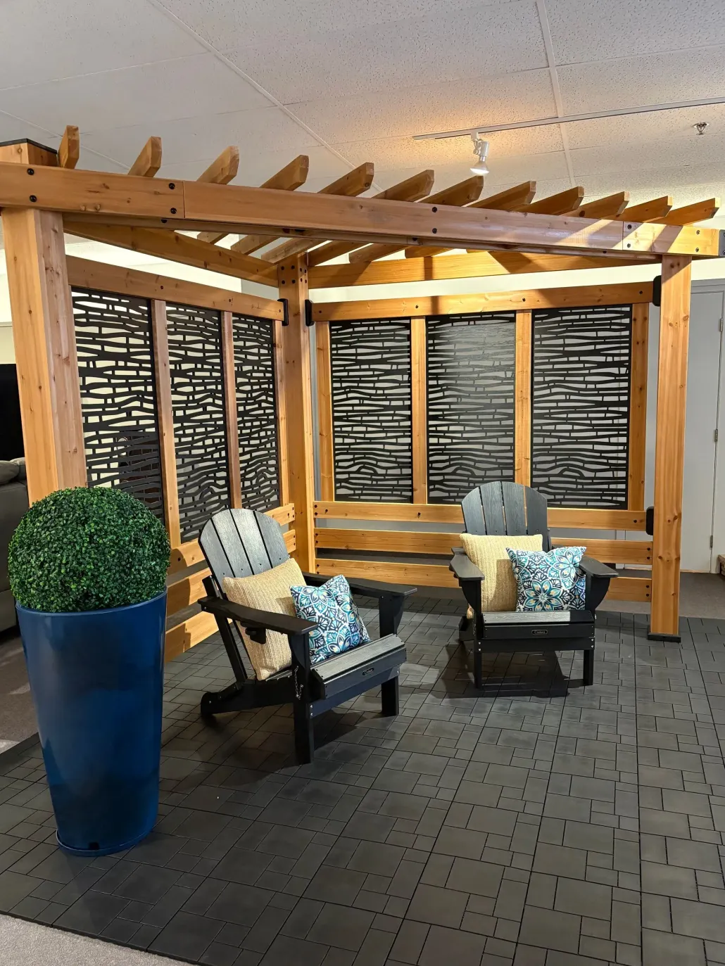 Covered patio seating area with two cushioned chairs, blue planter, and wooden pergola at sunset