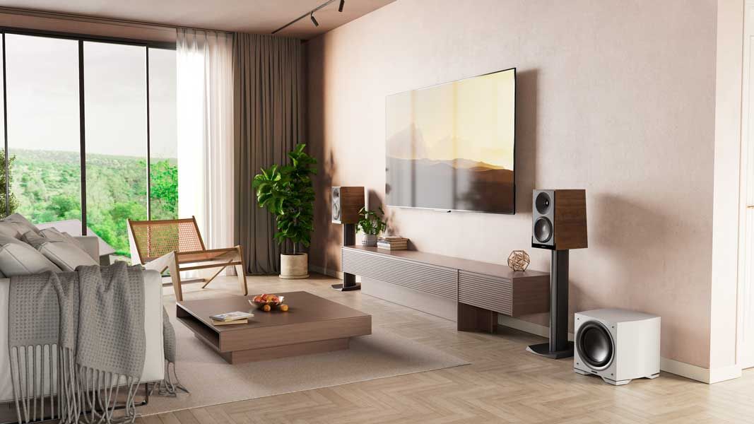 A living room with a couch, chair, coffee table, speakers and a flat screen tv.