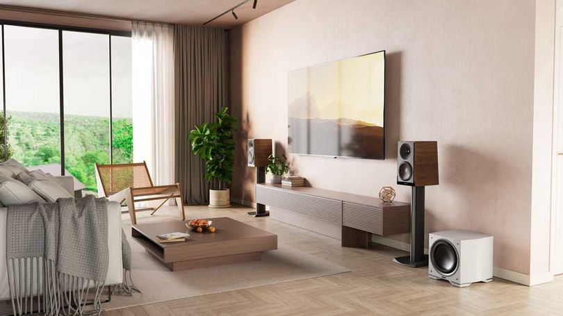 A living room with a couch, chair, coffee table, speakers and a flat screen tv.