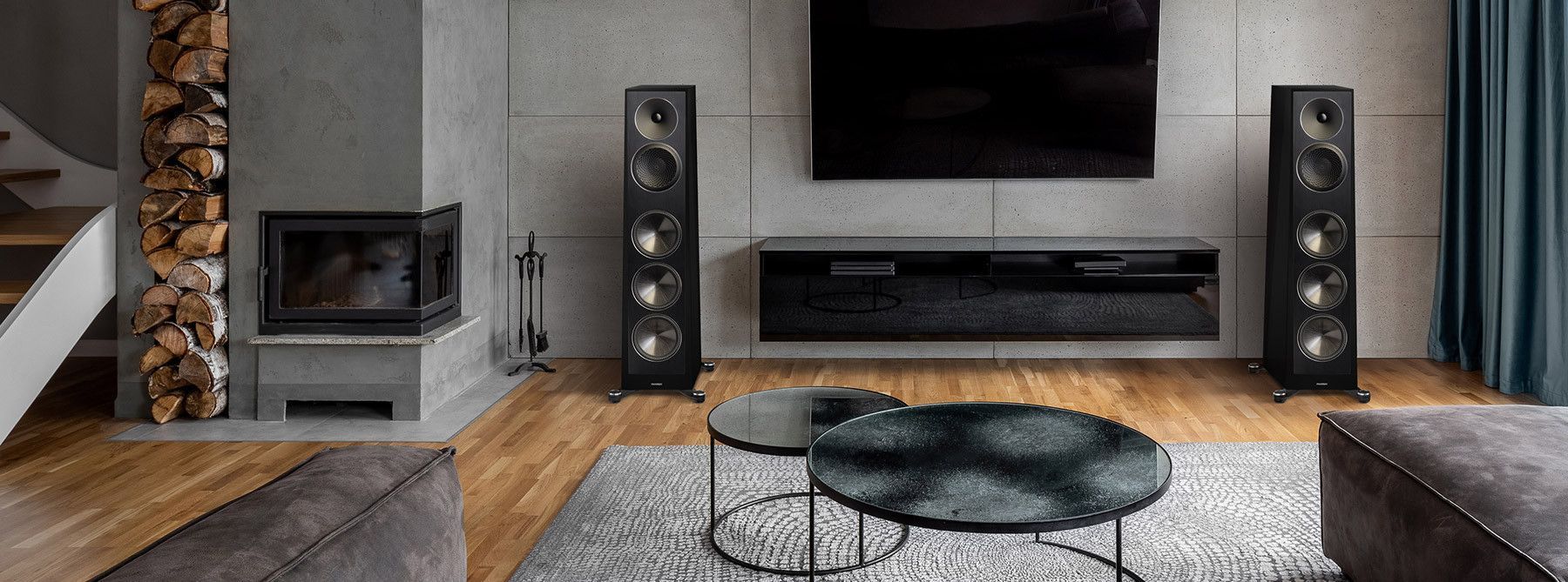 A living room with a flat screen tv , speakers , a coffee table and a fireplace.
