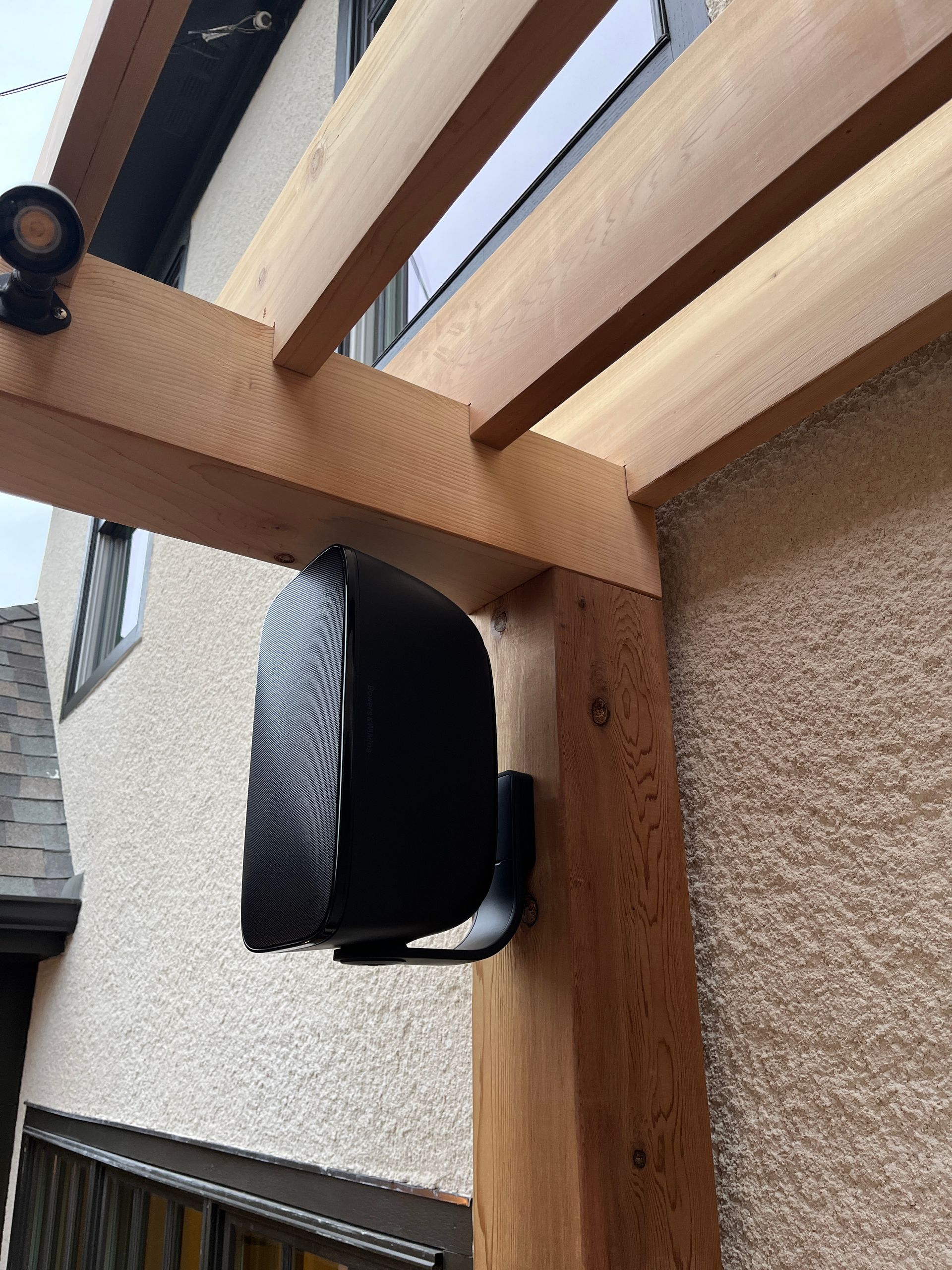 A speaker is mounted to a wooden structure on the side of a building.