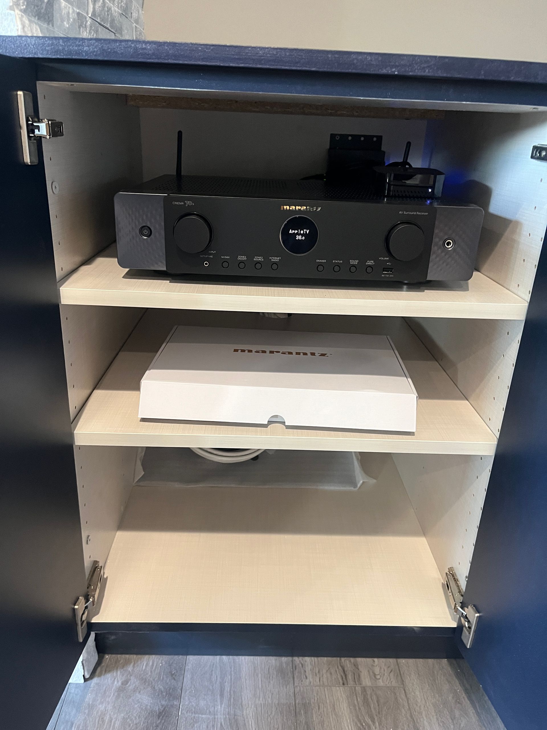 A black amplifier is sitting on top of a wooden shelf in a cabinet.