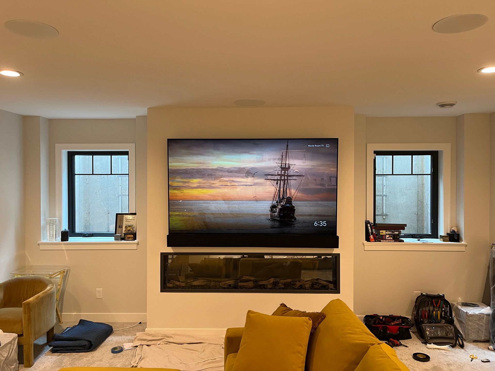 A living room with a yellow couch and a flat screen tv on the wall.