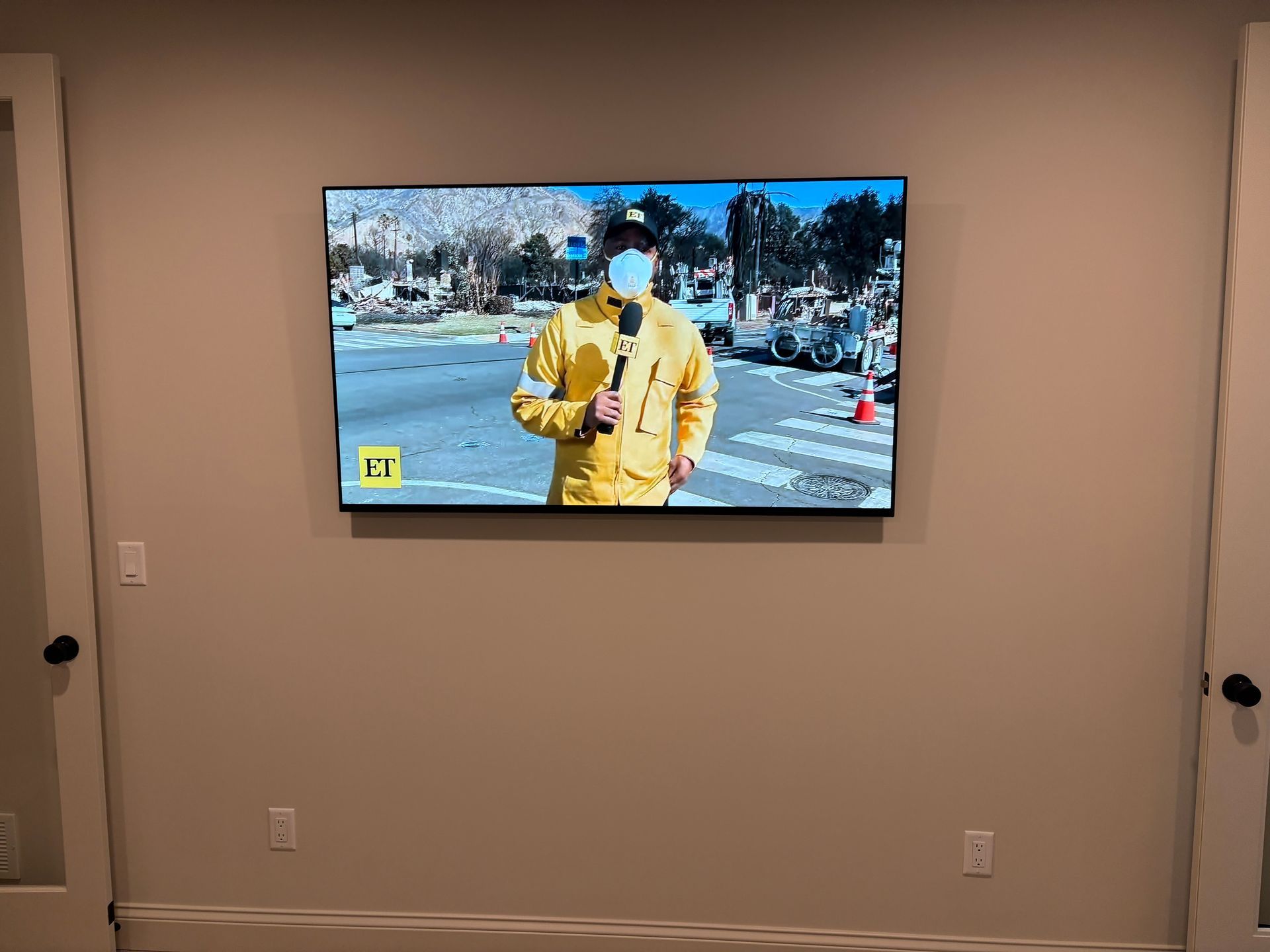 A television is hanging on a wall with a man in a yellow suit holding a microphone.