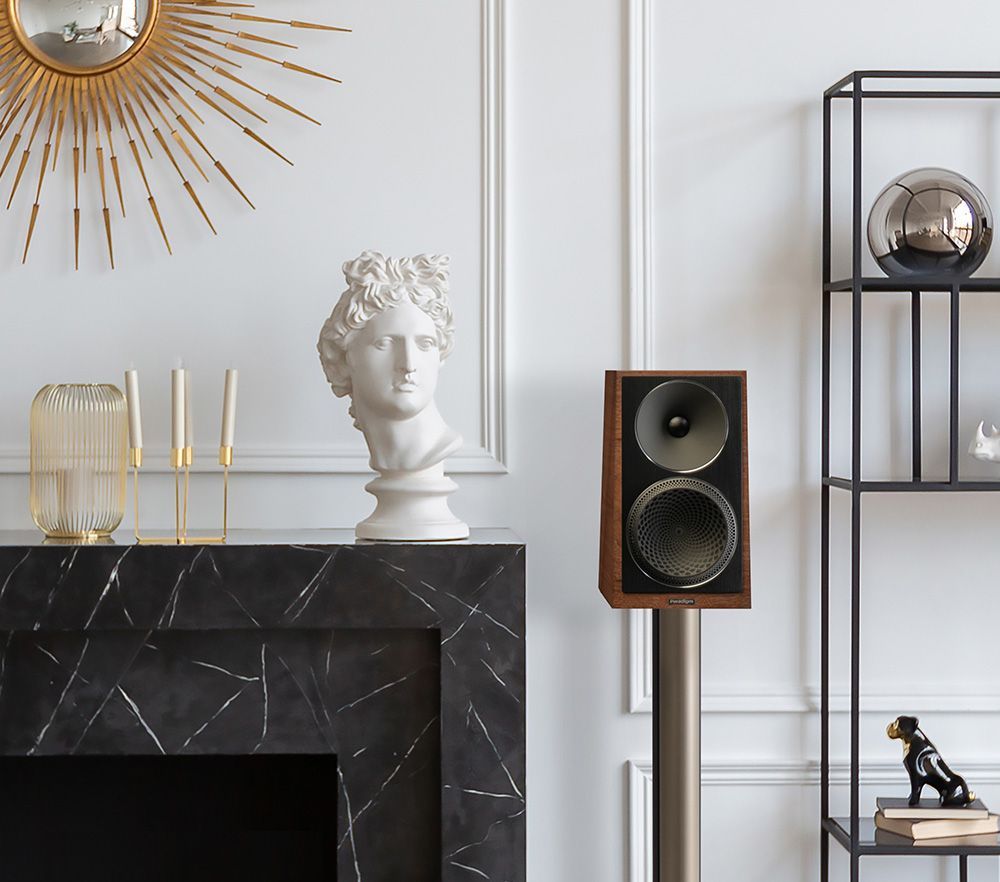 A living room with a fireplace , speakers , a statue and a mirror.