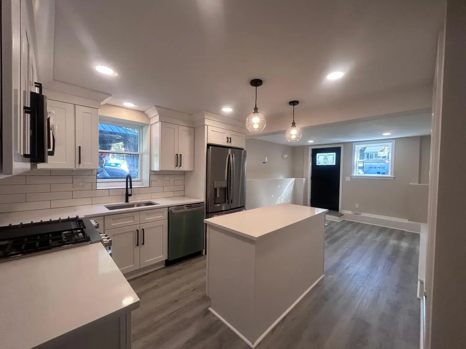 Newly renovated kitchen, white cabinets, island, stainless steel appliances, pendant lights, gray floor.