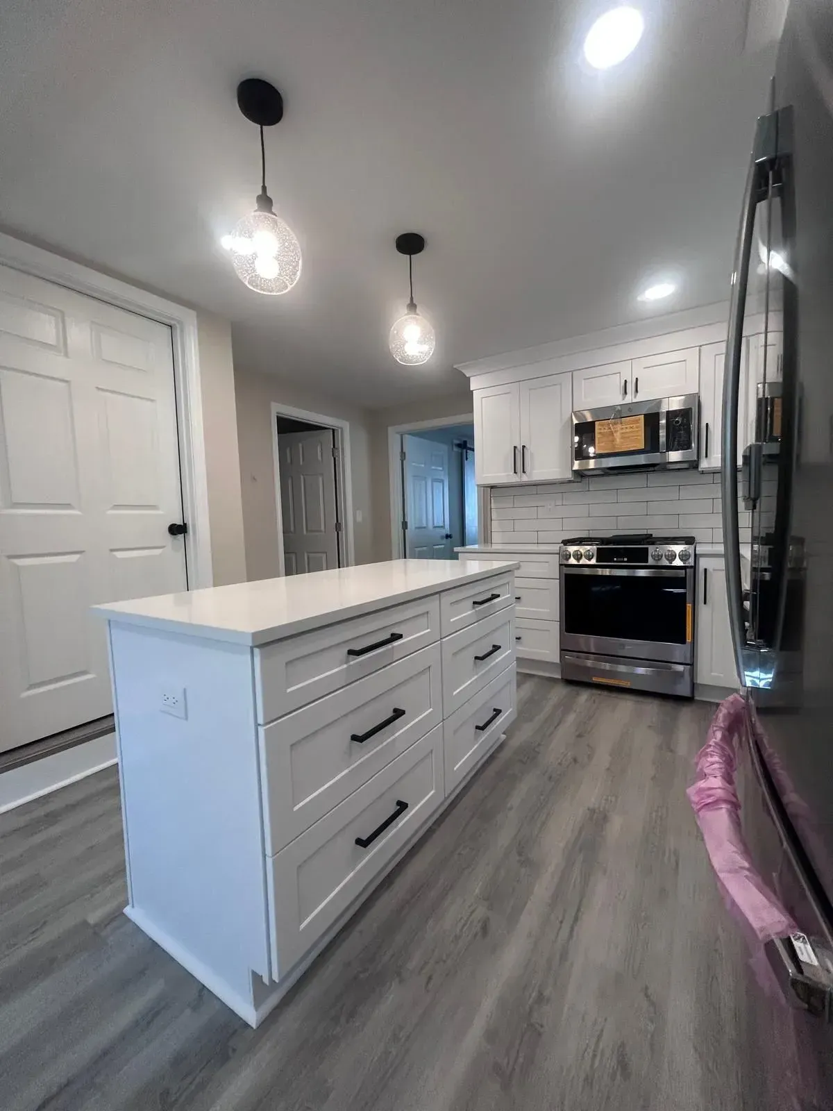 Modern white kitchen with island, gray floor, stainless steel appliances, and two hanging lights.