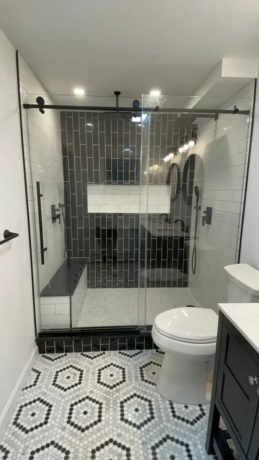 Modern bathroom with a glass shower, black and white tile, and a toilet.