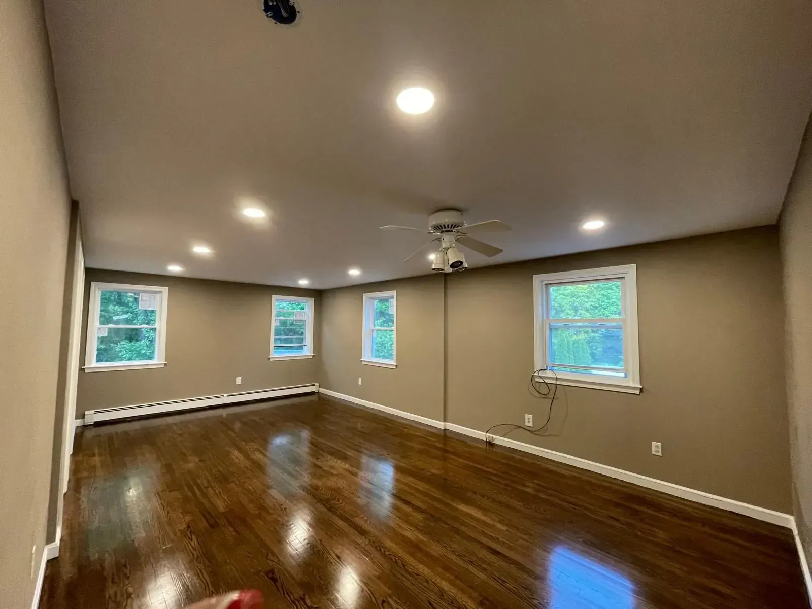Empty room with dark hardwood floors, tan walls, recessed lights, and windows.