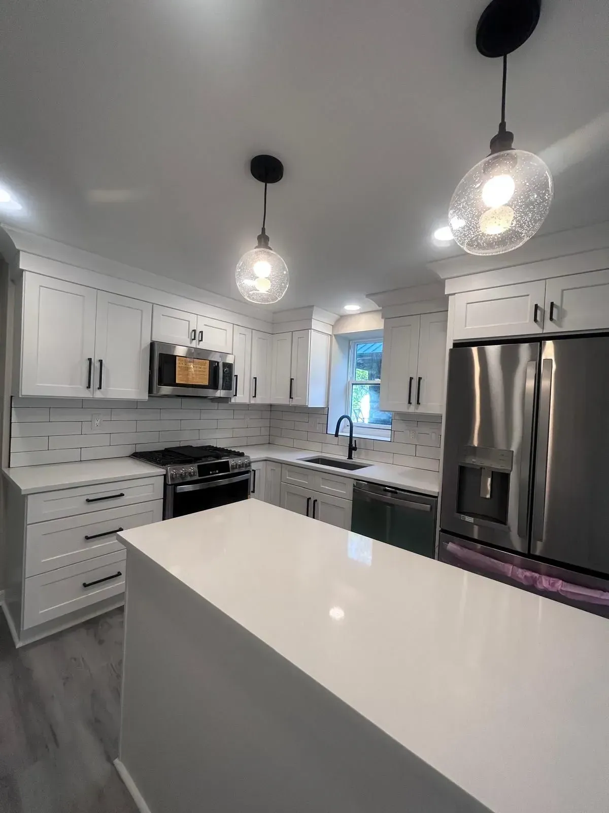 White modern kitchen with island, stainless steel appliances, and pendant lights.