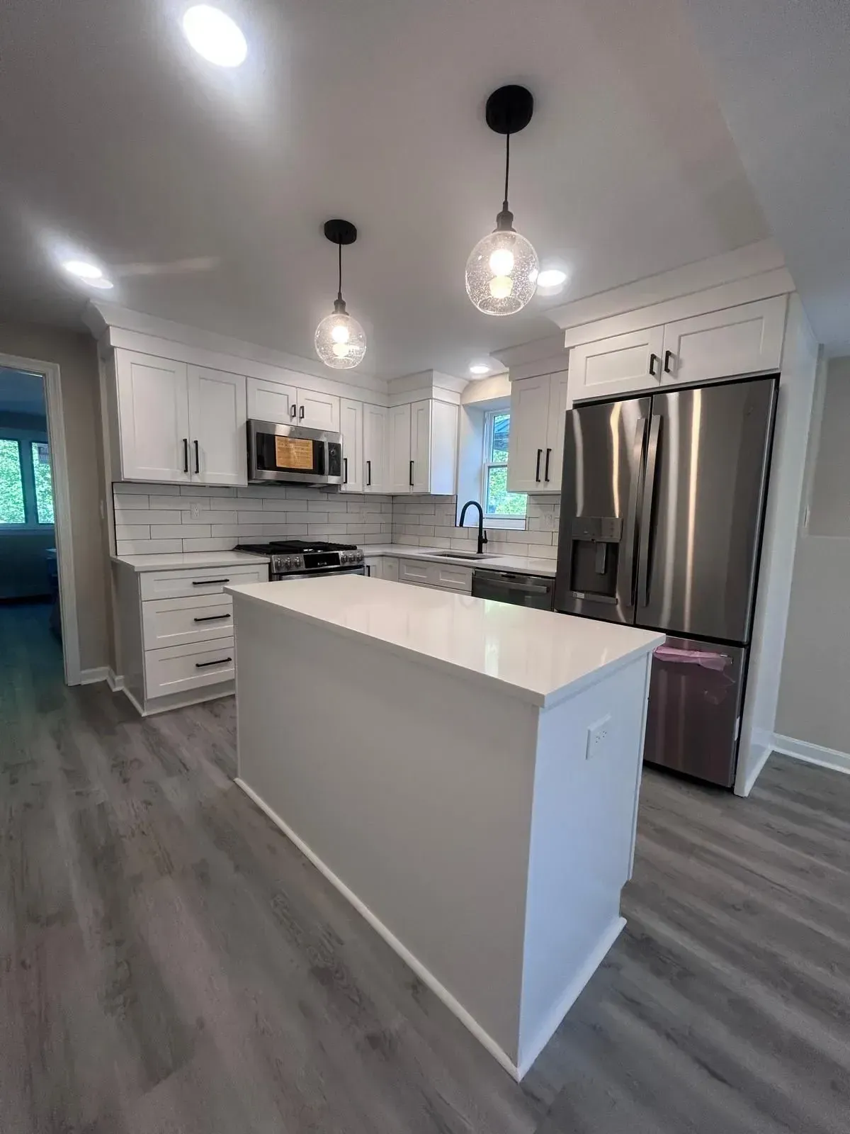 Modern white kitchen with island, stainless steel appliances, and gray flooring.