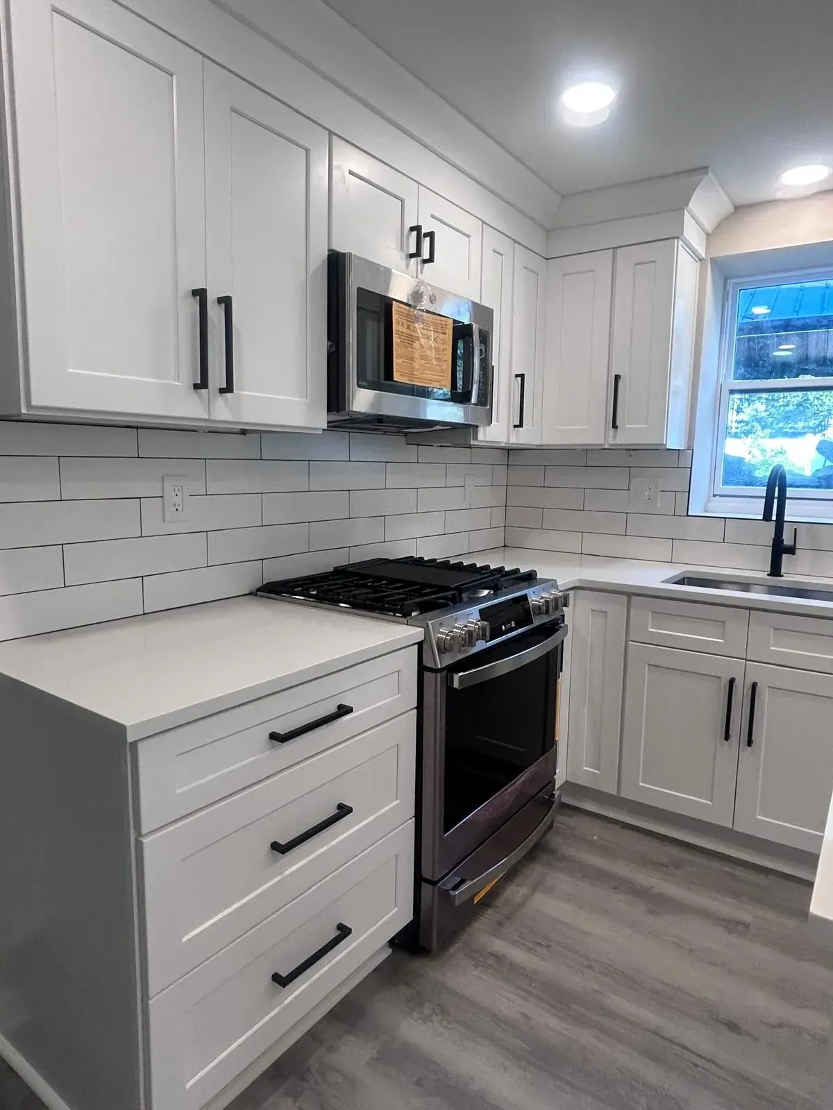 White kitchen with stainless steel appliances, white cabinets, and gray flooring.