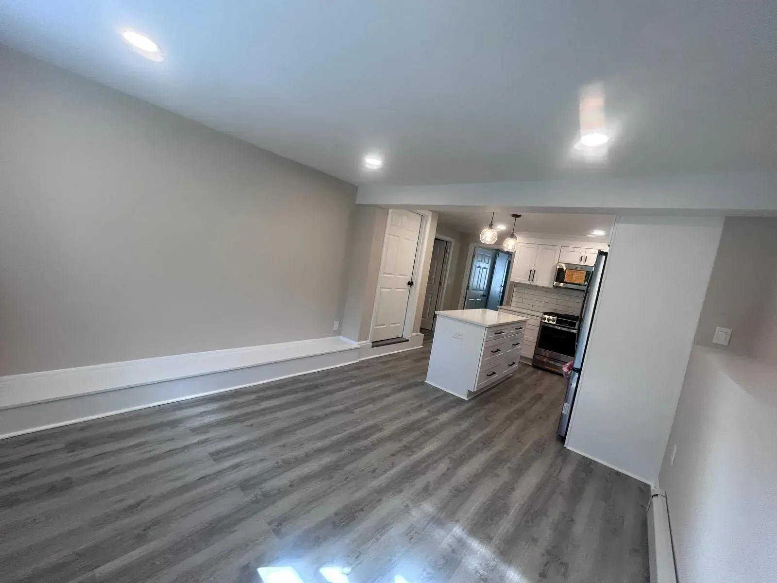 Empty living space with gray walls and flooring, opening into a kitchen with a white island.