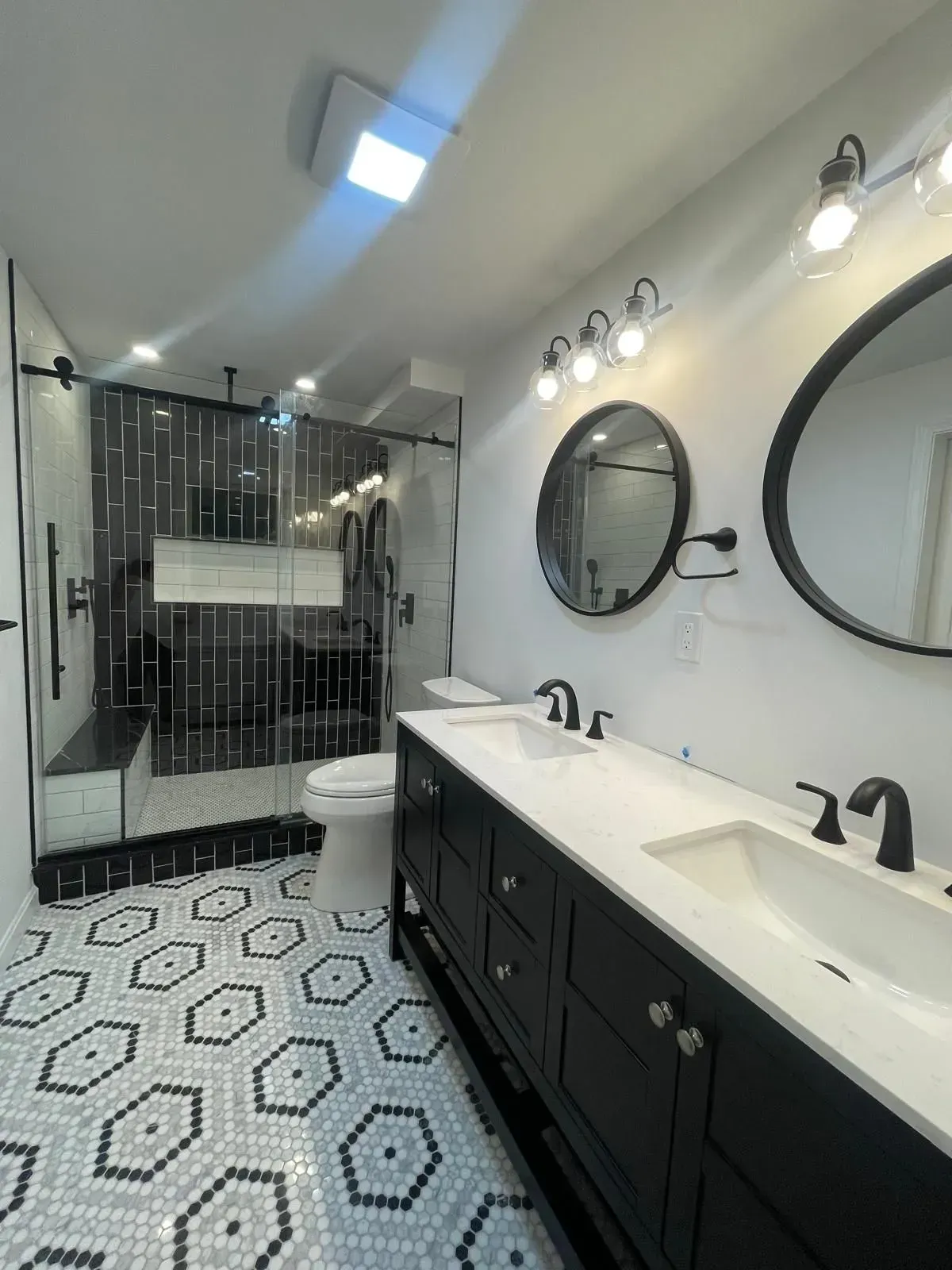 Modern bathroom with black vanity, white countertop, hexagon tile floor, and glass shower.