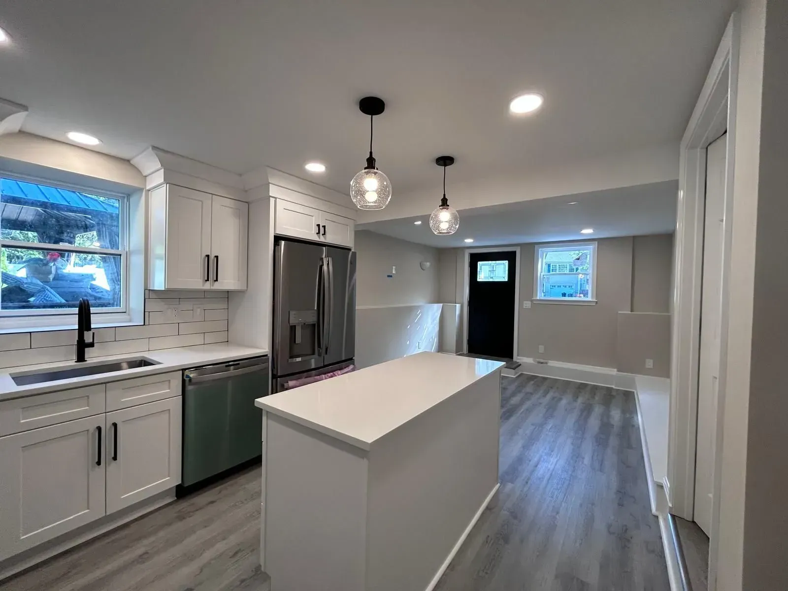 Modern kitchen with white cabinets, island, and stainless steel appliances; gray flooring.