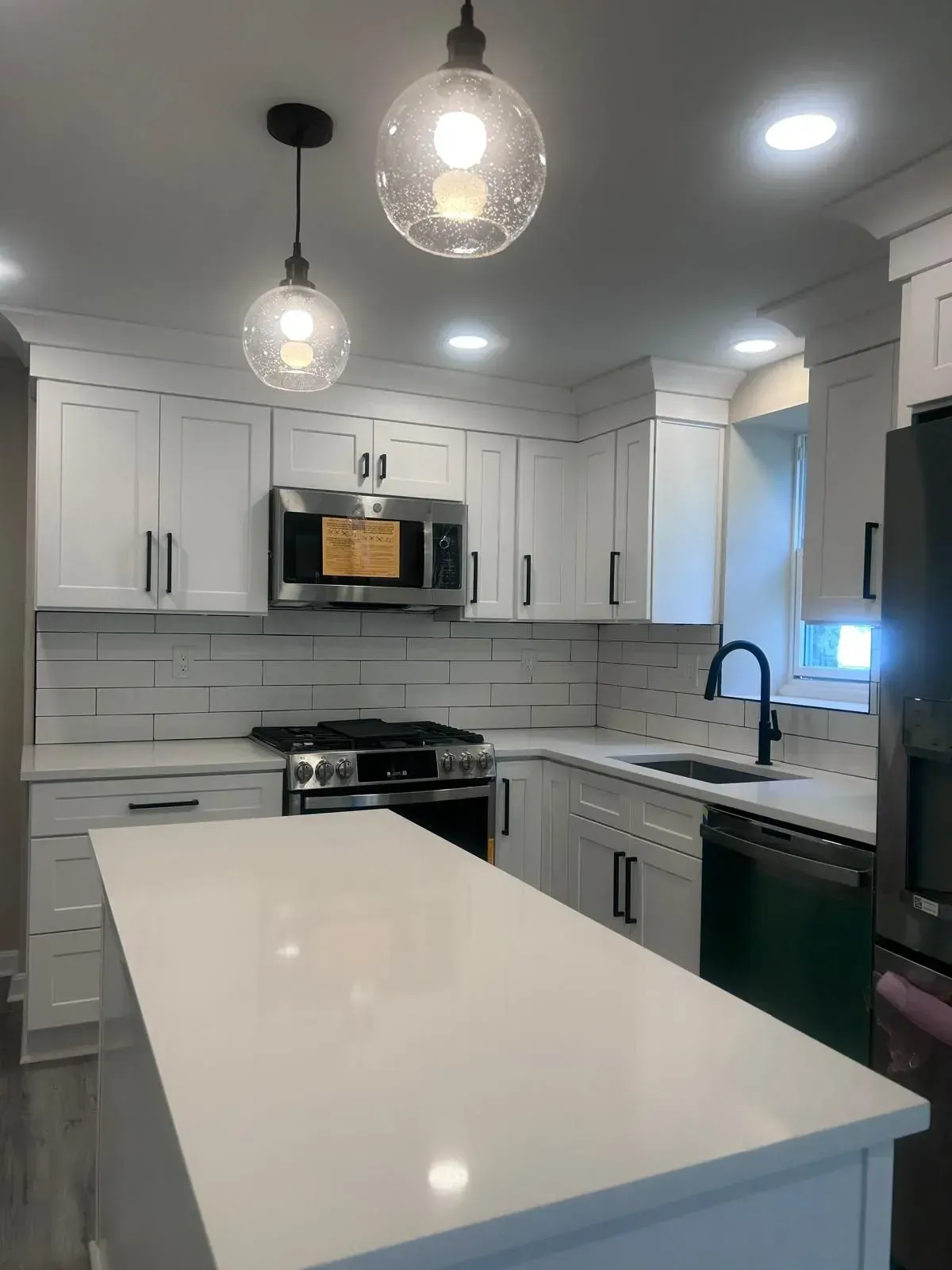 Modern white kitchen with island, black hardware, and pendant lights.